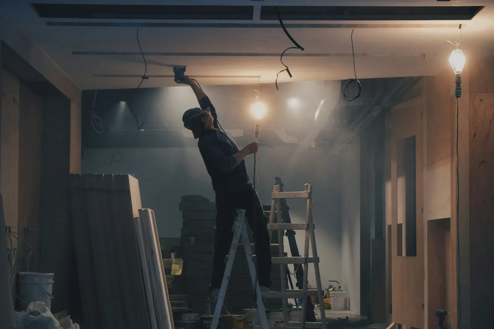 Travail d'un plafond en plaques de plâtre sur un chantier de rénovation, à la lumière des baladeuses